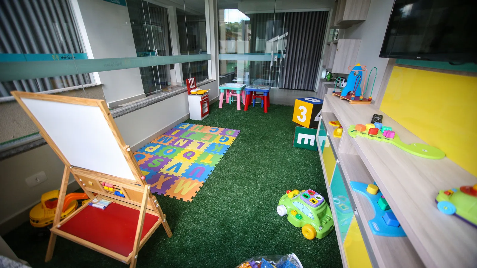 Sala de brincadeiras infantil iluminada, com brinquedos educativos organizados pelo chão e prateleiras baixas