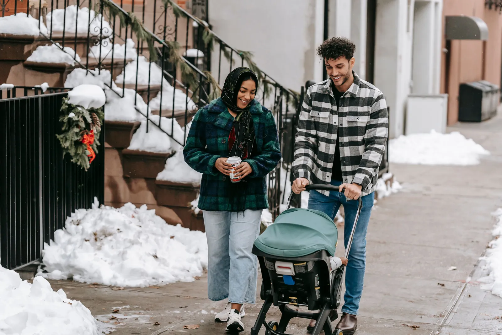 Casal passeando com um carrinho de bebê em uma calçada coberta de neve