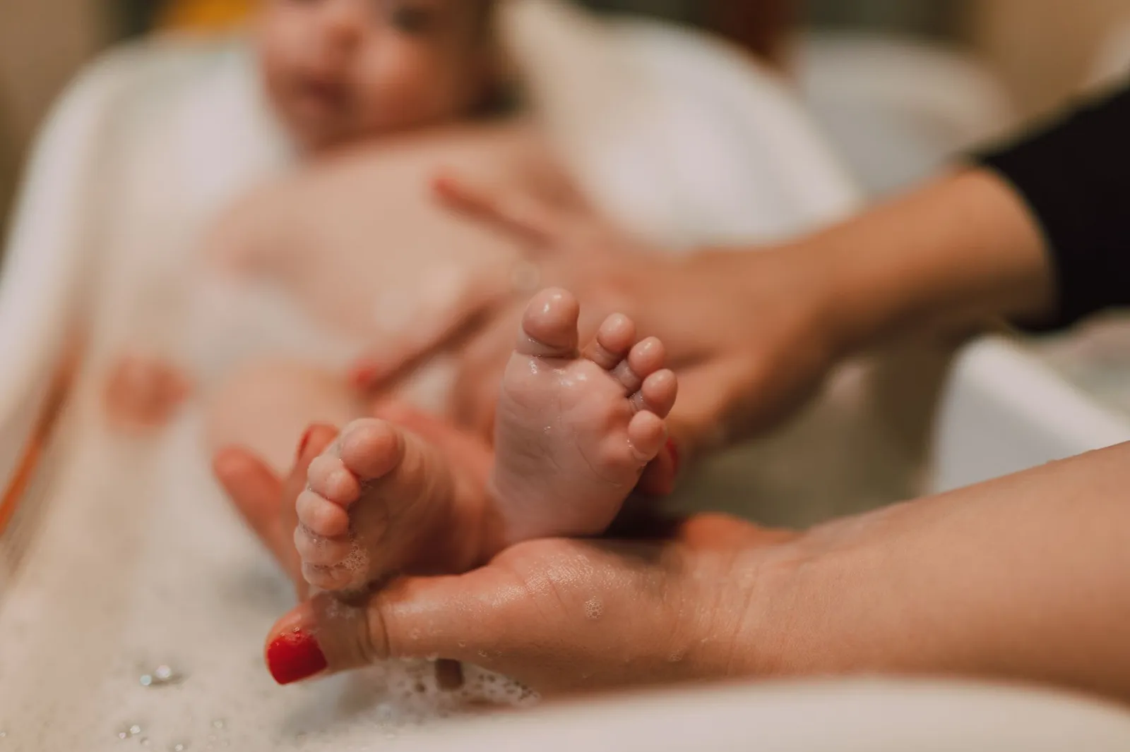 Pés de um bebê durante o banho, segurados com cuidado por mãos de adulto