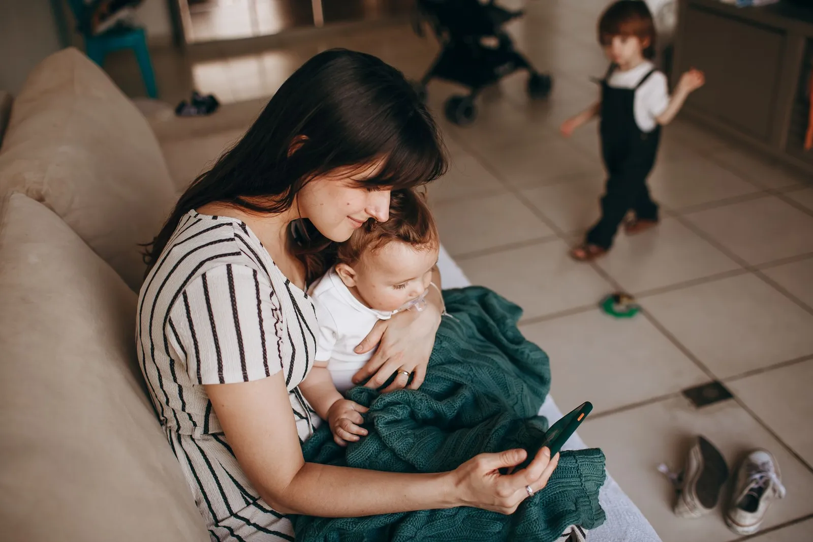 Mãe no sofá com o bebê no colo olhando o celular, imagem para o guia de como comprar fraldas online