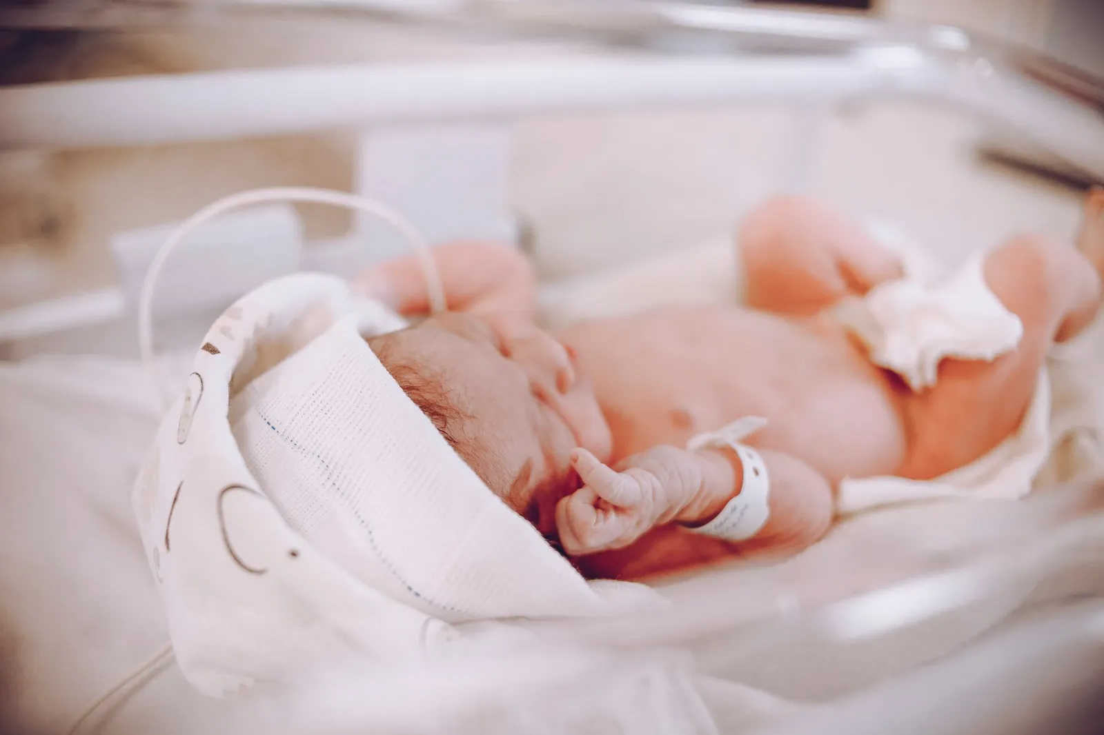 Recém-nascido prematuro com pulseira de identificação descansando em berço hospitalar