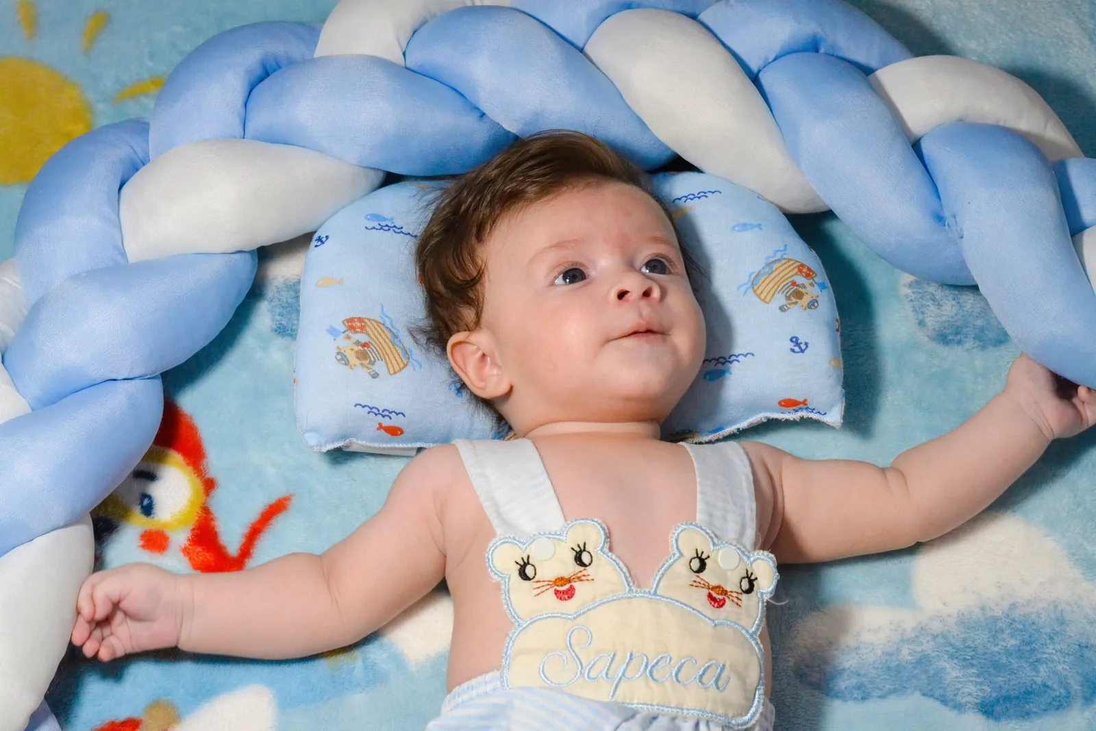 Bebê de body deitado sobre roupa de cama azul com estampa infantil