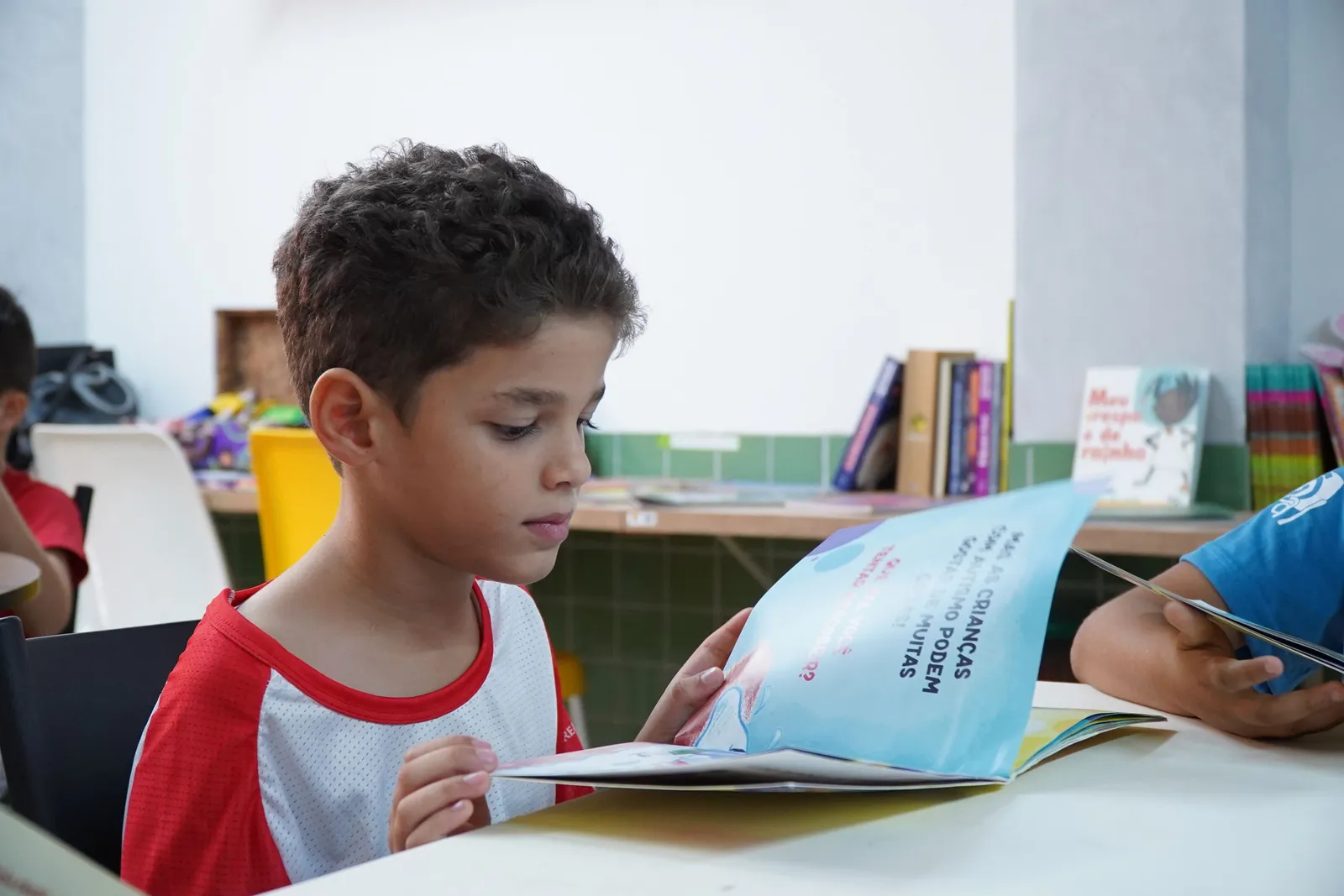Menino sentado lendo um livro, absorto na leitura em uma sala de aula