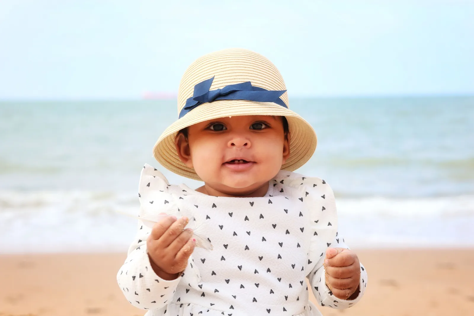 Bebê com chapéu e roupa estampada de corações aproveitando dia ensolarado na praia